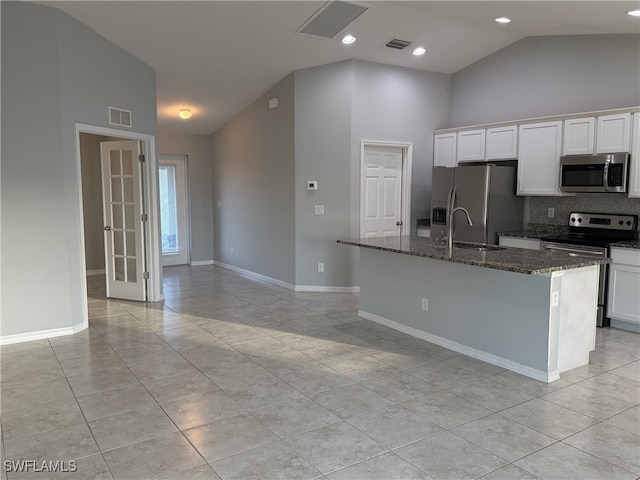 kitchen with dark stone countertops, a center island with sink, white cabinets, and stainless steel appliances