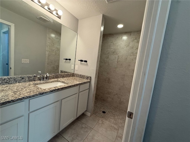 bathroom featuring vanity, a tile shower, a textured ceiling, and tile patterned flooring