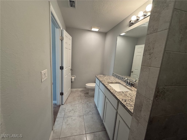 bathroom with tile patterned flooring, vanity, toilet, and a textured ceiling