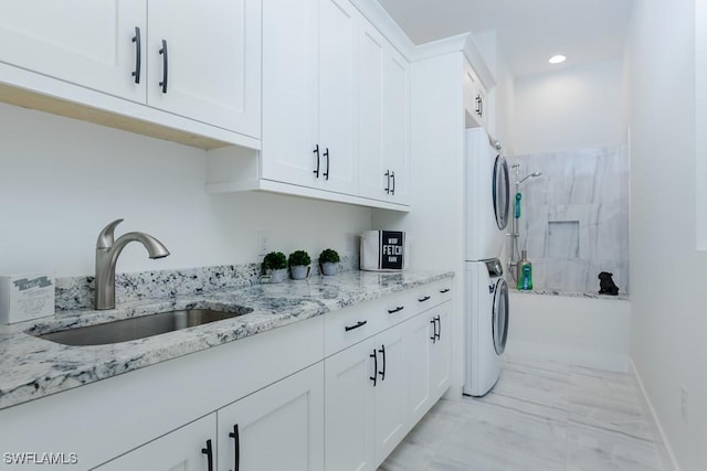 washroom featuring marble finish floor, stacked washer / drying machine, cabinet space, a sink, and baseboards