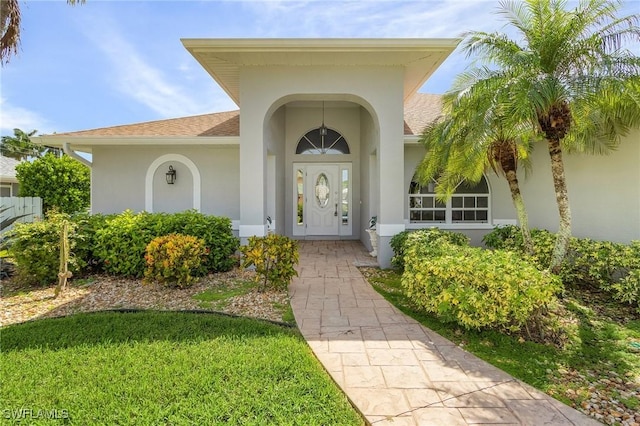 entrance to property featuring roof with shingles and stucco siding