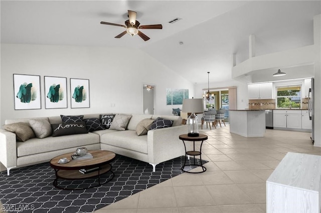 living area featuring ceiling fan with notable chandelier, high vaulted ceiling, light tile patterned flooring, and visible vents