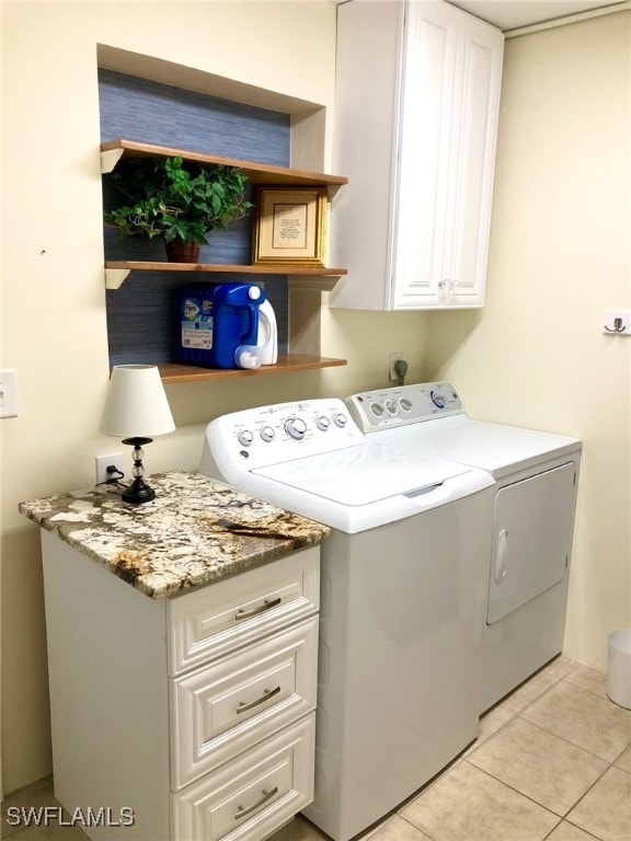 clothes washing area with washing machine and dryer, cabinets, and light tile patterned flooring