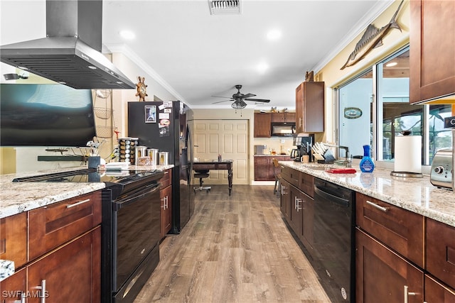 kitchen with light wood-type flooring, black appliances, wall chimney exhaust hood, ceiling fan, and ornamental molding