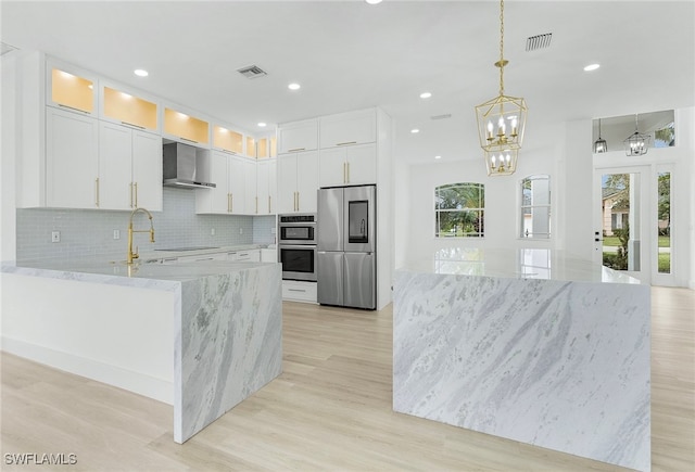 kitchen featuring appliances with stainless steel finishes, decorative light fixtures, white cabinetry, and wall chimney exhaust hood