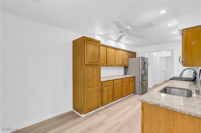 kitchen with stainless steel fridge, sink, ceiling fan, light stone counters, and light wood-type flooring