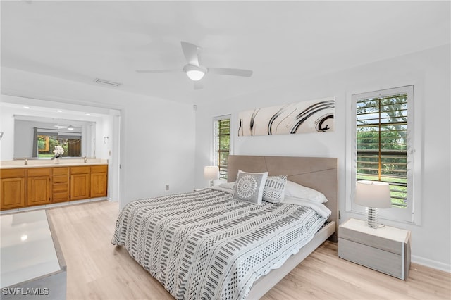 bedroom with multiple windows, ceiling fan, connected bathroom, and light hardwood / wood-style flooring