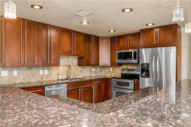 kitchen featuring hanging light fixtures, appliances with stainless steel finishes, sink, and dark stone counters