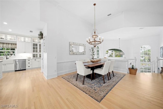 dining room with an inviting chandelier, a towering ceiling, and light wood-type flooring