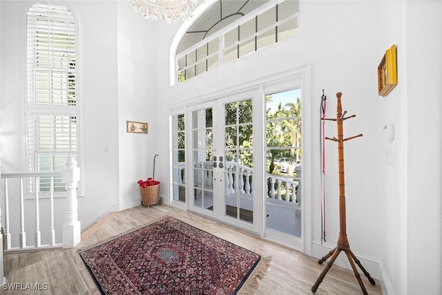 doorway to outside featuring a towering ceiling, light hardwood / wood-style flooring, french doors, and a notable chandelier