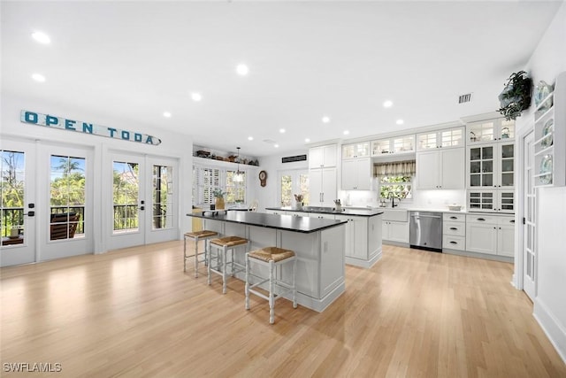 kitchen with light hardwood / wood-style floors, a kitchen breakfast bar, a kitchen island, stainless steel dishwasher, and white cabinets