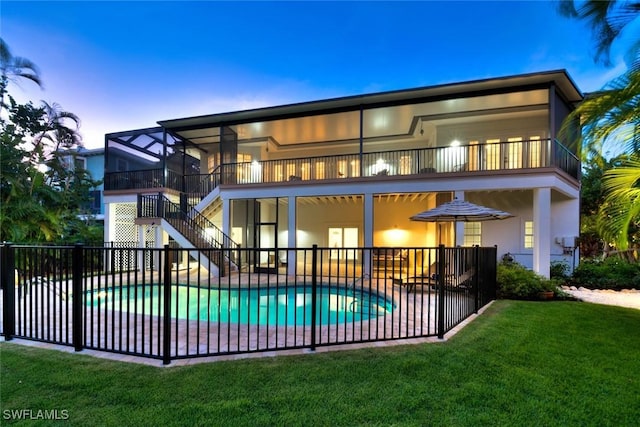 back house at dusk featuring a balcony, a fenced in pool, a lawn, and a patio