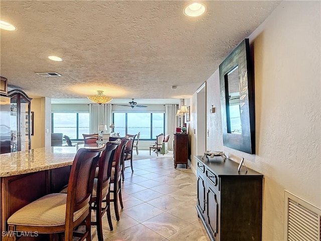 dining space with a textured ceiling, a textured wall, light tile patterned flooring, and visible vents