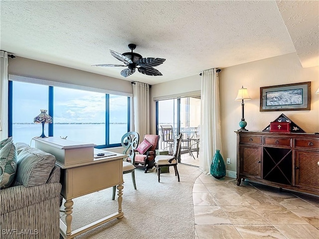 living room with a ceiling fan, a water view, light carpet, and a textured ceiling