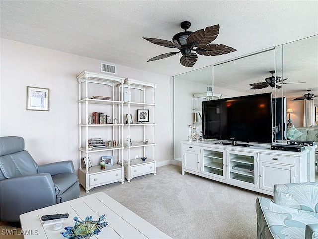 living room with a ceiling fan, visible vents, light colored carpet, and a textured ceiling