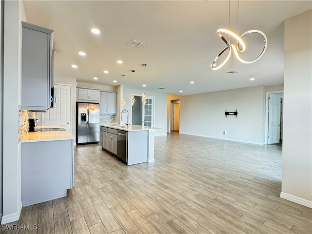 kitchen featuring hanging light fixtures, a center island with sink, light hardwood / wood-style flooring, stainless steel appliances, and decorative backsplash