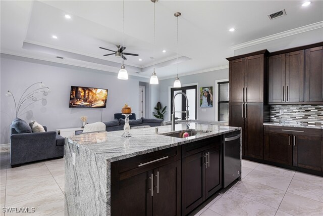 kitchen featuring stainless steel dishwasher, sink, light stone counters, a kitchen island with sink, and a tray ceiling