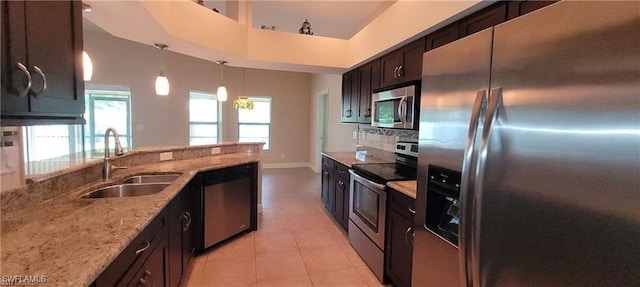 kitchen with light stone counters, pendant lighting, light tile patterned floors, sink, and stainless steel appliances