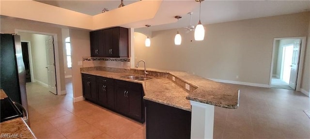 kitchen with sink, kitchen peninsula, decorative light fixtures, stainless steel refrigerator, and light stone countertops