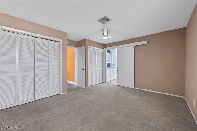 unfurnished bedroom featuring light colored carpet, ceiling fan, two closets, and connected bathroom