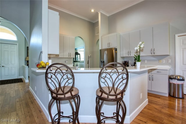 kitchen with hardwood / wood-style floors, stainless steel fridge, arched walkways, a breakfast bar area, and light countertops