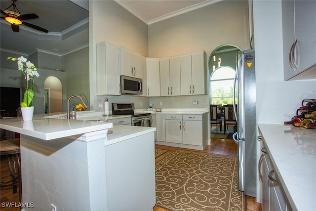 kitchen featuring stainless steel appliances, dark hardwood / wood-style flooring, a kitchen breakfast bar, ceiling fan, and ornamental molding