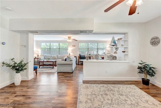 living room with built in features, wood-type flooring, plenty of natural light, and ceiling fan