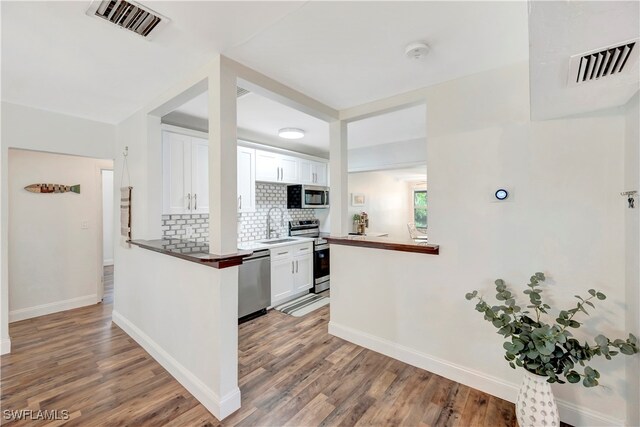 kitchen with appliances with stainless steel finishes, tasteful backsplash, white cabinetry, and wood-type flooring