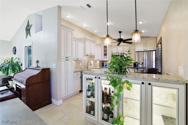 kitchen with stainless steel fridge, decorative light fixtures, light stone counters, decorative backsplash, and vaulted ceiling