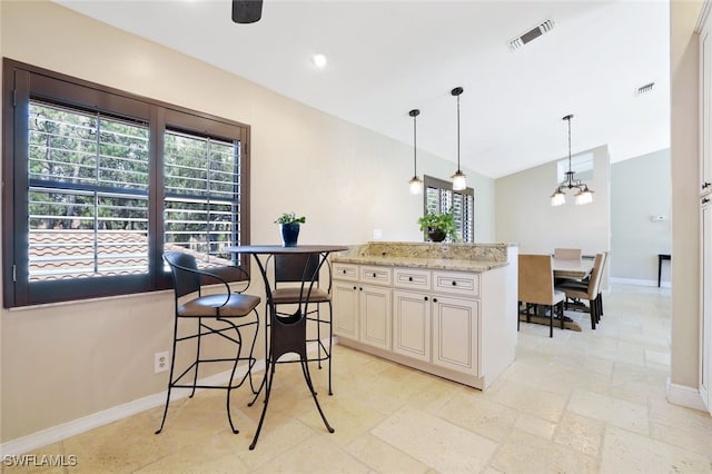 kitchen featuring pendant lighting, a kitchen breakfast bar, an inviting chandelier, a center island, and light stone countertops