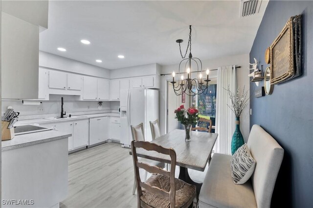 kitchen with white appliances, light wood finished floors, white cabinetry, light countertops, and a notable chandelier