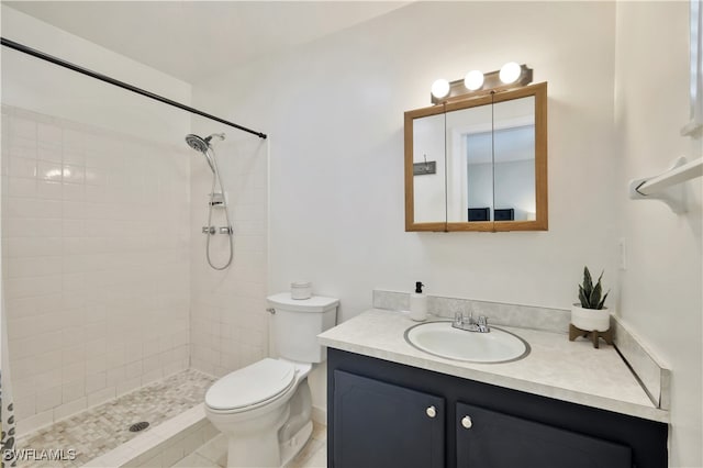 bathroom with toilet, a tile shower, and vanity