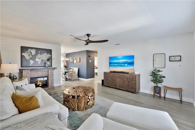 living room featuring a ceiling fan, baseboards, a fireplace, and wood finished floors