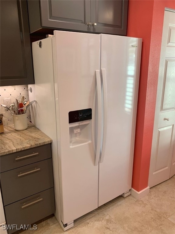 kitchen featuring white fridge with ice dispenser, backsplash, and light stone counters