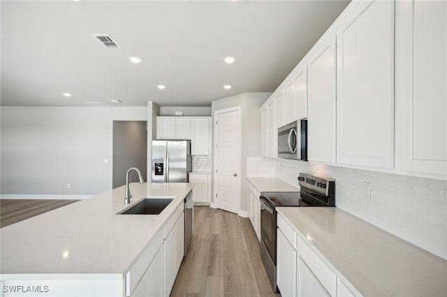 kitchen with light stone counters, sink, white cabinetry, light hardwood / wood-style flooring, and appliances with stainless steel finishes