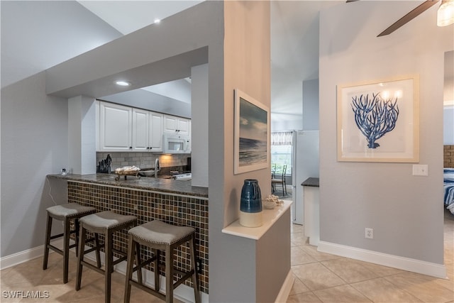 kitchen featuring a kitchen bar, ceiling fan, tasteful backsplash, light tile patterned flooring, and white cabinets