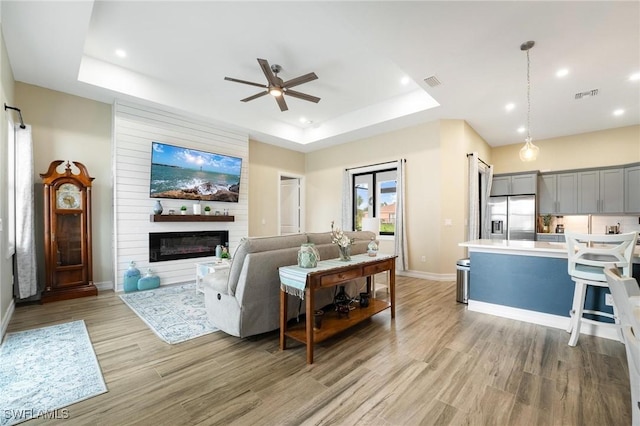 living room featuring a raised ceiling, ceiling fan, a fireplace, and light hardwood / wood-style floors