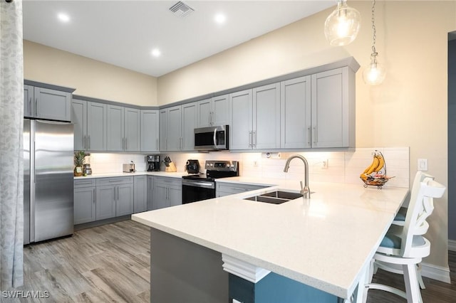 kitchen featuring sink, a kitchen breakfast bar, kitchen peninsula, decorative light fixtures, and appliances with stainless steel finishes