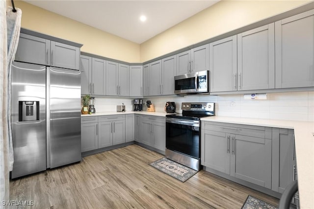 kitchen featuring gray cabinets, decorative backsplash, stainless steel appliances, and light wood-type flooring