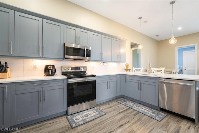 kitchen with backsplash, sink, decorative light fixtures, light hardwood / wood-style floors, and stainless steel appliances