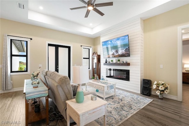 living room with dark hardwood / wood-style flooring, ceiling fan, and a raised ceiling