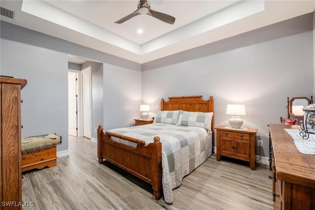 bedroom featuring a tray ceiling, ceiling fan, and light wood-type flooring