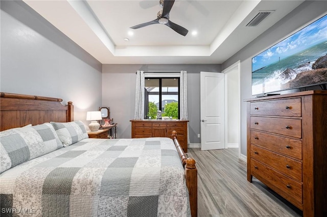 bedroom featuring ceiling fan, light hardwood / wood-style floors, and a tray ceiling