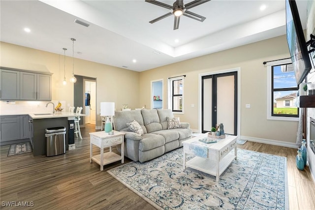 living room featuring a tray ceiling, dark hardwood / wood-style flooring, ceiling fan, and sink