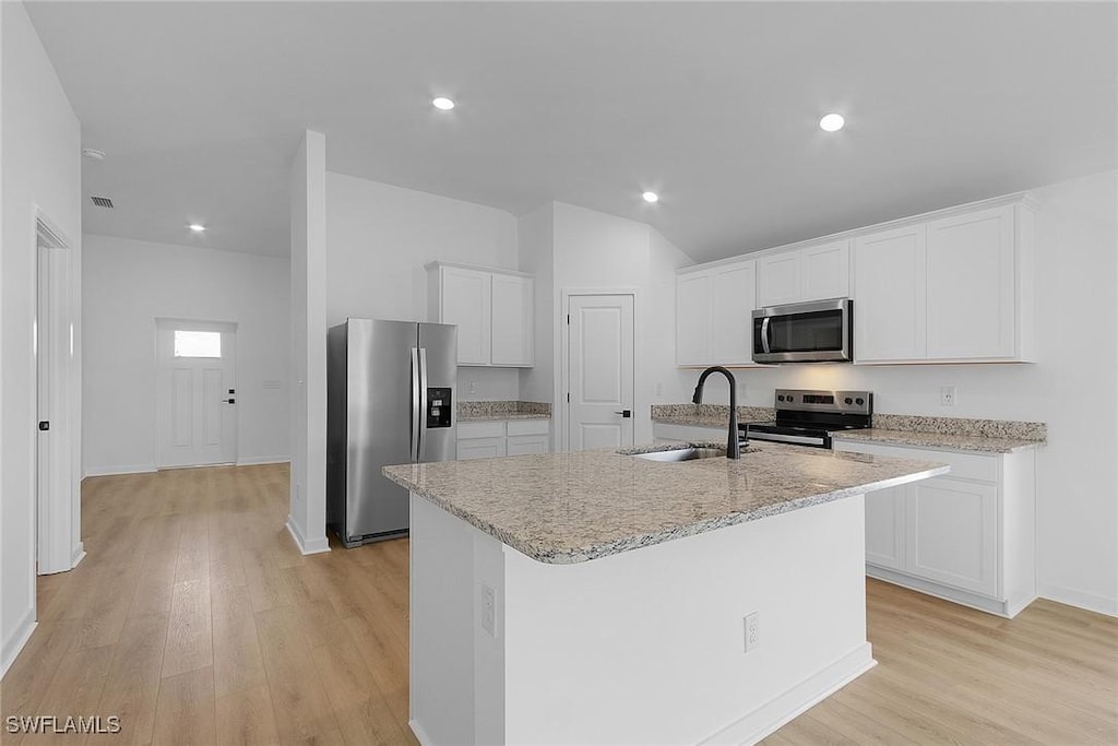 1313 Bush St W, Immokalee, FL 34142 - kitchen featuring appliances with stainless steel finishes, a sink, light wood-style floors, white cabinets, and an island with sink
