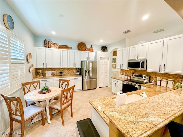 kitchen featuring light stone countertops, backsplash, stainless steel appliances, white cabinets, and light tile patterned flooring