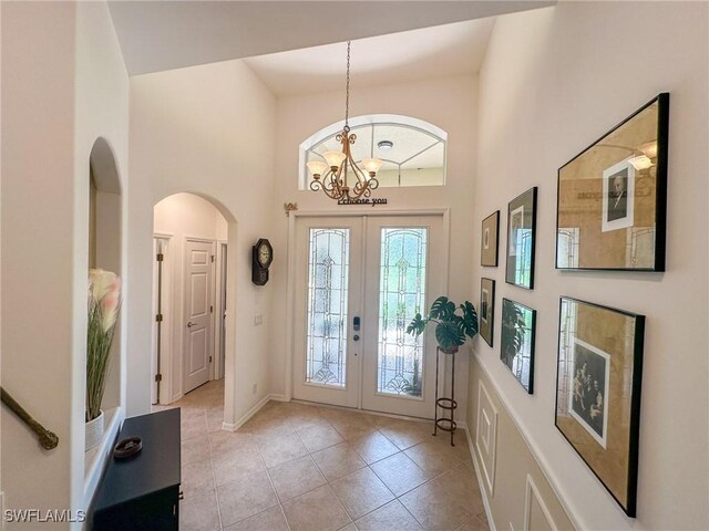 tiled entryway with french doors, an inviting chandelier, and a high ceiling