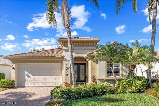 mediterranean / spanish house featuring an attached garage, a tiled roof, french doors, decorative driveway, and stucco siding