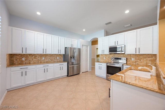 kitchen featuring light stone counters, arched walkways, appliances with stainless steel finishes, white cabinetry, and a sink