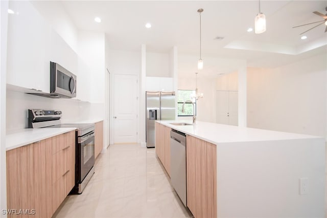 kitchen with decorative light fixtures, a kitchen island with sink, white cabinetry, a raised ceiling, and stainless steel appliances